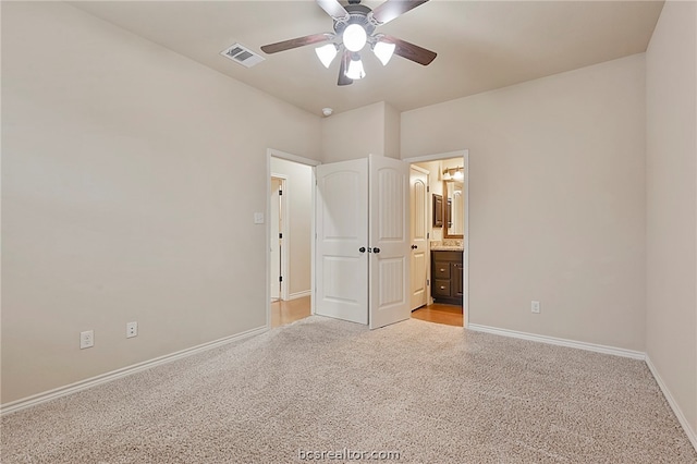 unfurnished bedroom featuring light carpet, ensuite bathroom, baseboards, visible vents, and a ceiling fan