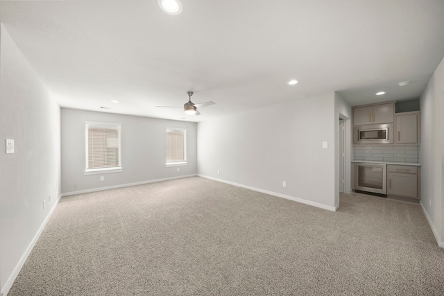 unfurnished living room with ceiling fan, light colored carpet, and baseboards