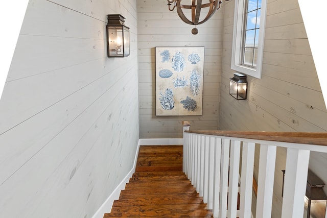 staircase featuring a chandelier, wood finished floors, and wooden walls