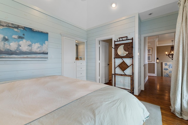 bedroom featuring wood walls, wood finished floors, and an inviting chandelier