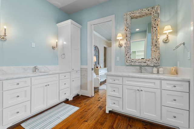 full bath featuring two vanities, a wainscoted wall, wood-type flooring, and a sink