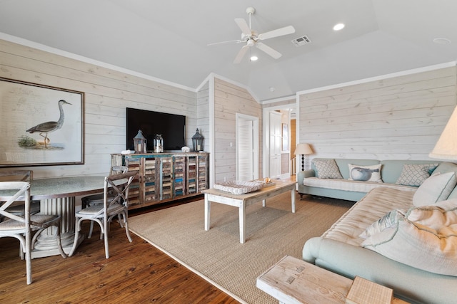 living area with lofted ceiling, a ceiling fan, visible vents, wood walls, and wood finished floors