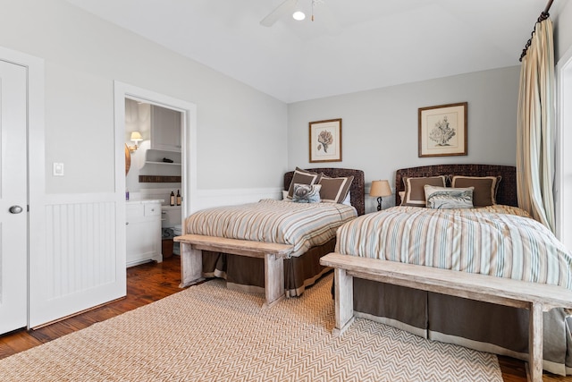 bedroom featuring wood finished floors, a ceiling fan, ensuite bath, and wainscoting
