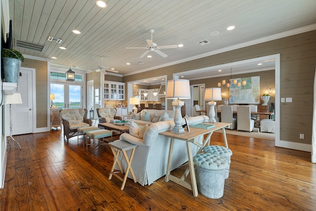 living area featuring wooden walls, wood-type flooring, visible vents, and ceiling fan with notable chandelier