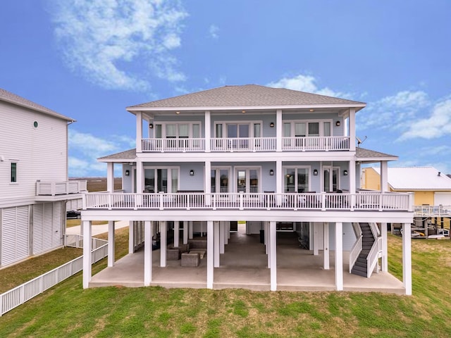 rear view of property with a lawn, roof with shingles, a balcony, and a patio