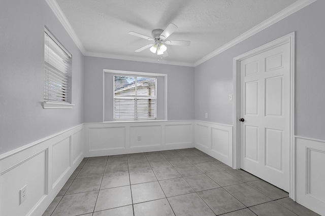 empty room with light tile patterned flooring, crown molding, a ceiling fan, a textured ceiling, and wainscoting