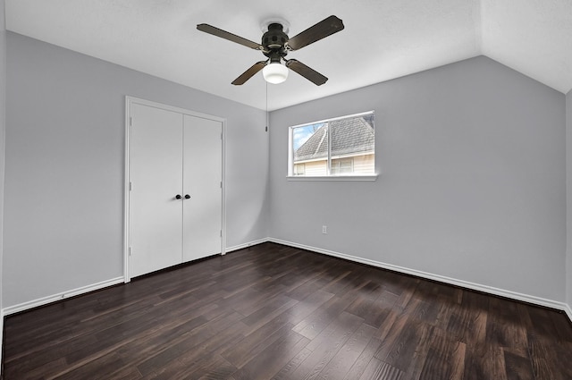 unfurnished bedroom featuring dark wood finished floors, a closet, vaulted ceiling, baseboards, and a ceiling fan