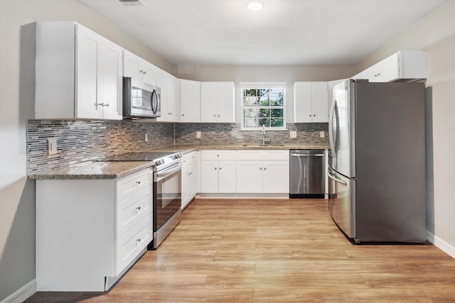 kitchen featuring light stone countertops, stainless steel appliances, backsplash, light wood finished floors, and white cabinetry