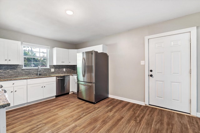 kitchen with a sink, appliances with stainless steel finishes, baseboards, wood finished floors, and backsplash