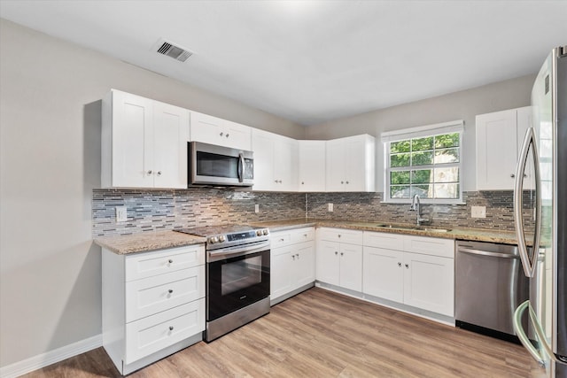 kitchen featuring light stone countertops, stainless steel appliances, light wood-type flooring, a sink, and visible vents