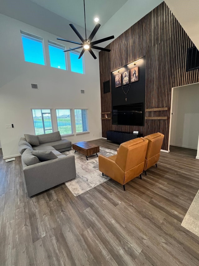 living room with a towering ceiling, a ceiling fan, visible vents, and wood finished floors