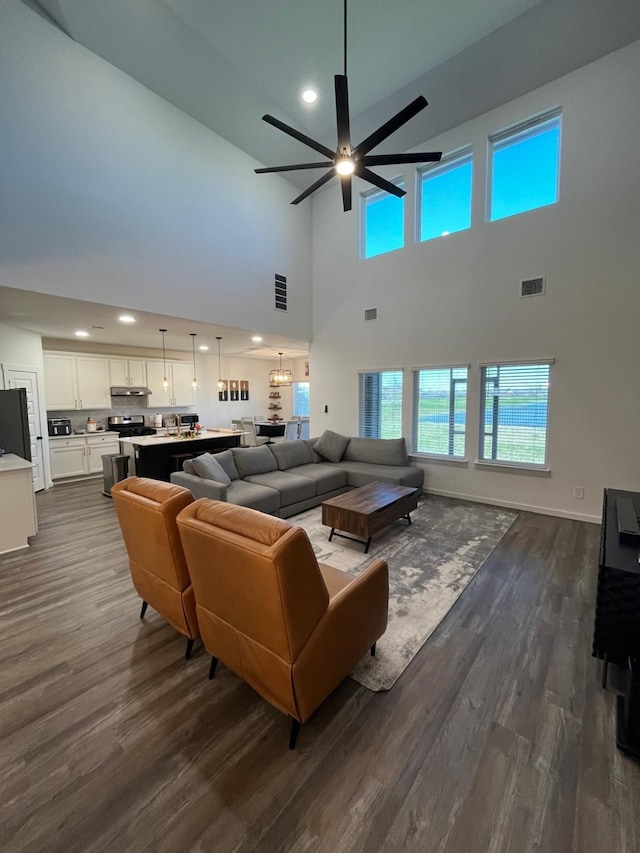 living area featuring a high ceiling, dark wood-style flooring, a healthy amount of sunlight, a ceiling fan, and visible vents