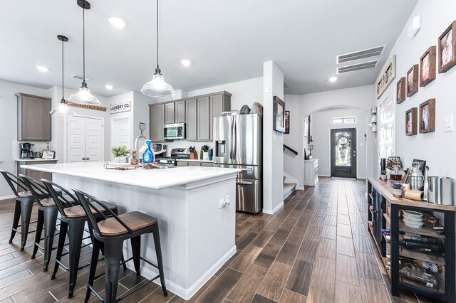 kitchen featuring dark wood-style floors, a breakfast bar area, light countertops, arched walkways, and appliances with stainless steel finishes