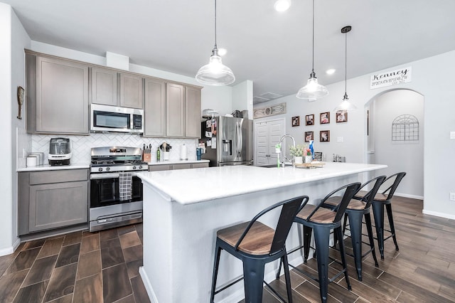 kitchen featuring tasteful backsplash, appliances with stainless steel finishes, light countertops, baseboards, and arched walkways