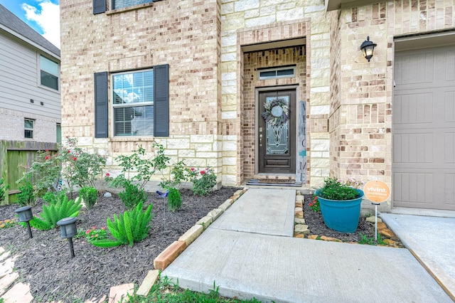 doorway to property featuring a garage, brick siding, fence, and stone siding