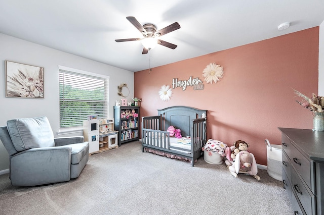 carpeted bedroom with ceiling fan and a nursery area