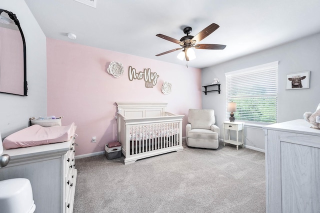 carpeted bedroom featuring a ceiling fan, a nursery area, and baseboards