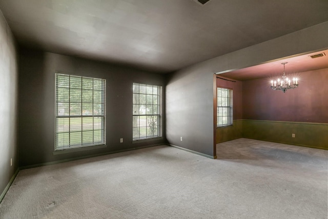 carpeted spare room featuring visible vents, wainscoting, and an inviting chandelier