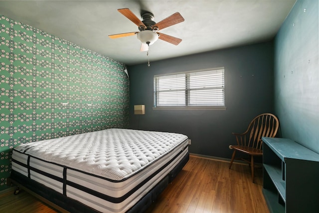 bedroom with baseboards, an accent wall, wallpapered walls, and wood finished floors