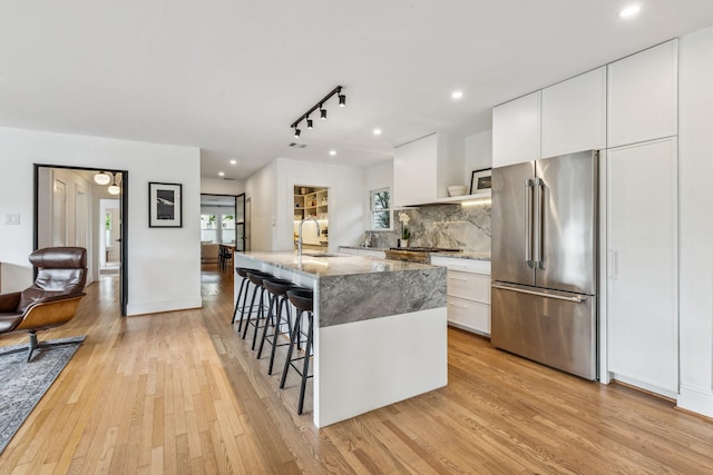 1202 Ashland St, Houston, TX 77008 - kitchen featuring high end fridge, light wood-style floors, a breakfast bar area, an island with sink, and light stone countertops