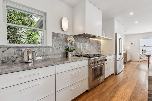 1202 Ashland St, Houston, TX 77008 - kitchen with high end appliances, wall chimney range hood, decorative backsplash, white cabinets, and recessed lighting