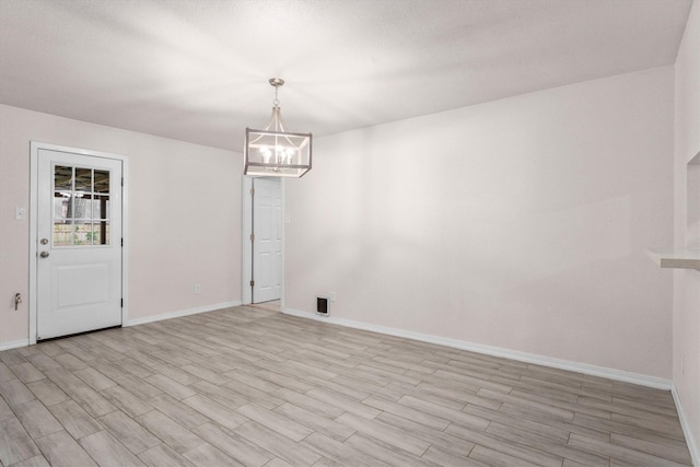 unfurnished dining area with a notable chandelier, light wood-style flooring, and baseboards