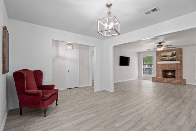 living area featuring a brick fireplace, visible vents, light wood-style flooring, baseboards, and ceiling fan with notable chandelier