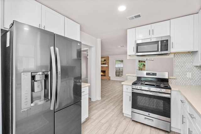 kitchen with decorative backsplash, white cabinets, appliances with stainless steel finishes, visible vents, and light countertops