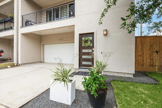 entrance to property featuring driveway, a balcony, stucco siding, fence, and a garage