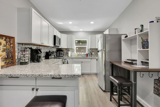 1315 Kilgore Rd, Baytown, TX 77520 - kitchen with white cabinets, appliances with stainless steel finishes, light wood-style flooring, a peninsula, and decorative backsplash