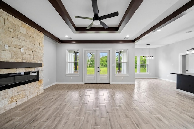 unfurnished living room with a raised ceiling, a healthy amount of sunlight, a stone fireplace, and ceiling fan with notable chandelier