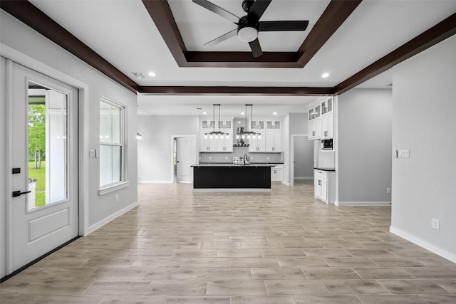 unfurnished living room featuring recessed lighting, baseboards, a raised ceiling, and ceiling fan with notable chandelier