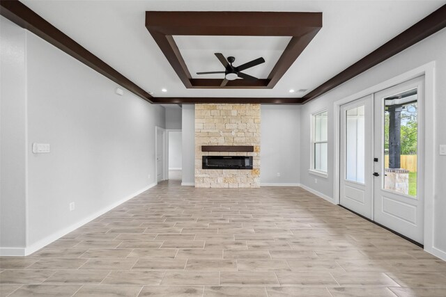 unfurnished living room with a ceiling fan, a stone fireplace, baseboards, and a tray ceiling