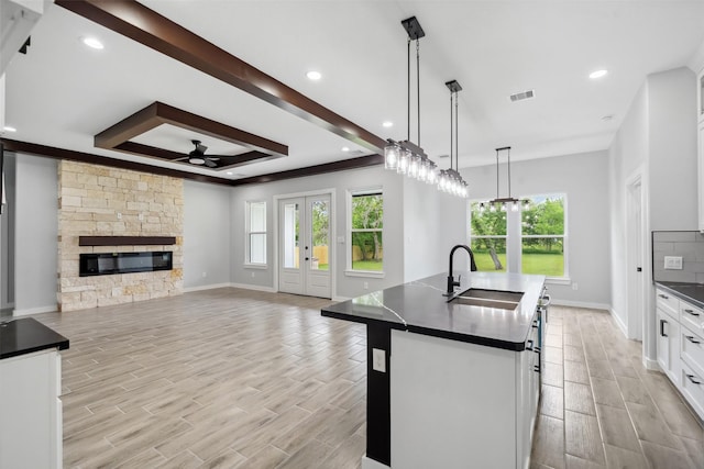kitchen featuring a sink, dark countertops, ceiling fan, visible vents, and an island with sink