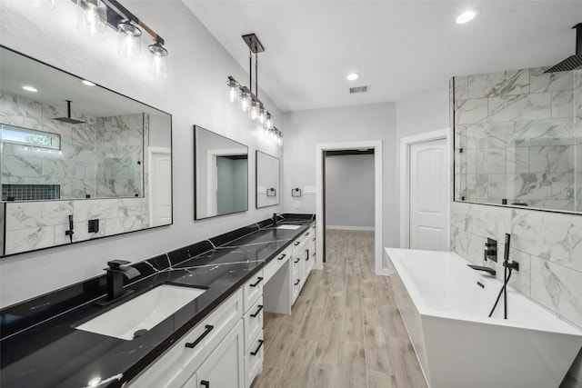 full bathroom with visible vents, a tile shower, a freestanding bath, and a sink