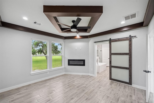 unfurnished living room featuring a ceiling fan, visible vents, a barn door, and a tray ceiling
