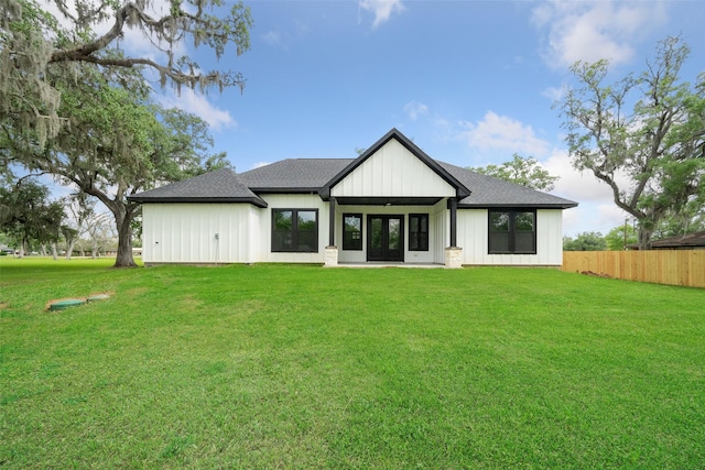 rear view of house featuring a yard, a shingled roof, and fence