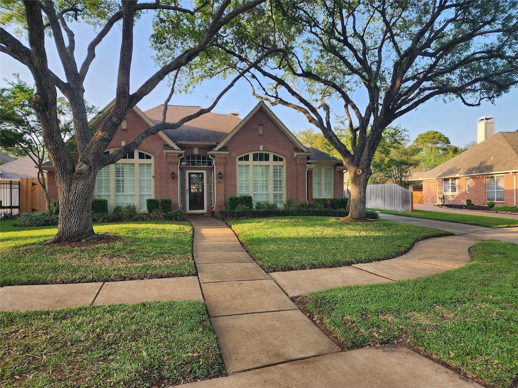 view of front facade with brick siding, fence, and a front lawn