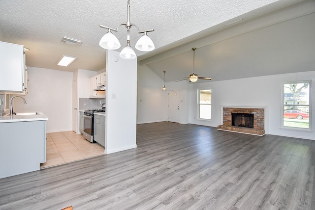 kitchen featuring lofted ceiling, a sink, visible vents, light countertops, and stainless steel gas range oven
