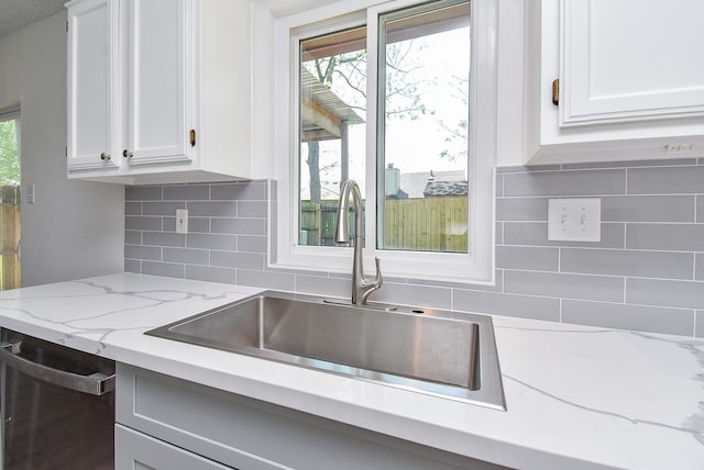 kitchen with tasteful backsplash, stainless steel dishwasher, light stone counters, white cabinets, and a sink