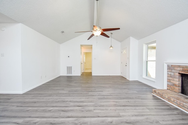 unfurnished living room featuring ceiling fan, visible vents, vaulted ceiling, a fireplace, and wood finished floors