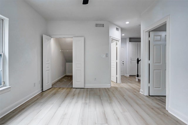 unfurnished bedroom featuring visible vents, a spacious closet, a closet, and light wood-style flooring