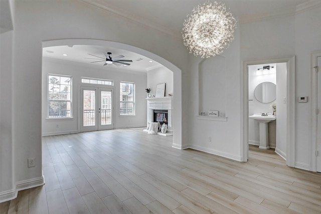 unfurnished living room with light wood-type flooring, crown molding, baseboards, and ceiling fan with notable chandelier
