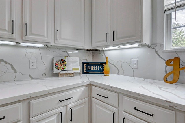 kitchen with light stone countertops, decorative backsplash, and white cabinets