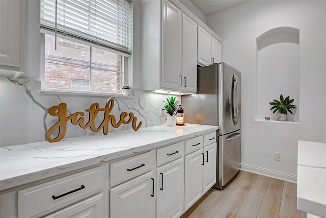 kitchen with tasteful backsplash, light stone countertops, light wood-style floors, white cabinets, and baseboards