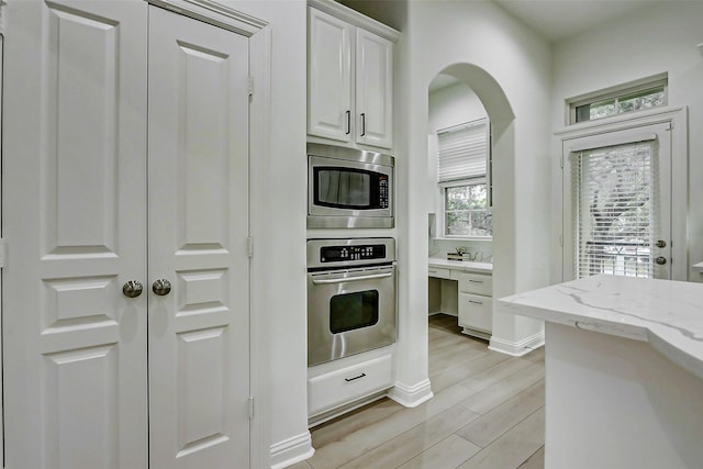 kitchen featuring light stone countertops, stainless steel appliances, light wood-type flooring, arched walkways, and white cabinets