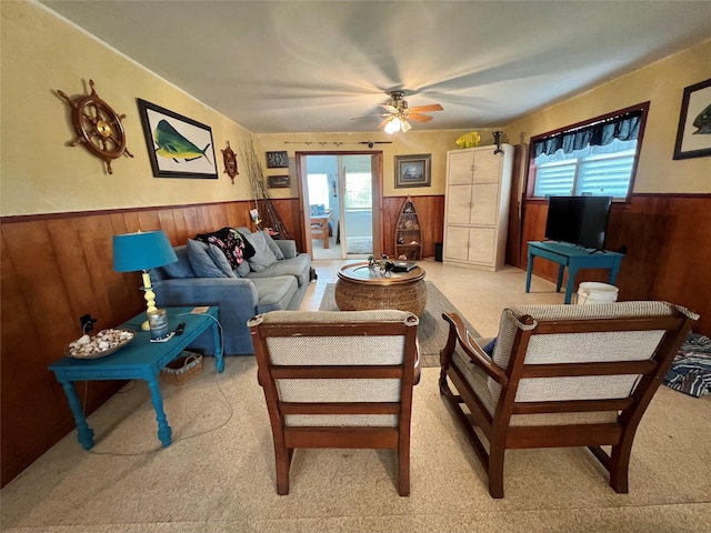 living area featuring wooden walls, a wainscoted wall, ceiling fan, and a healthy amount of sunlight
