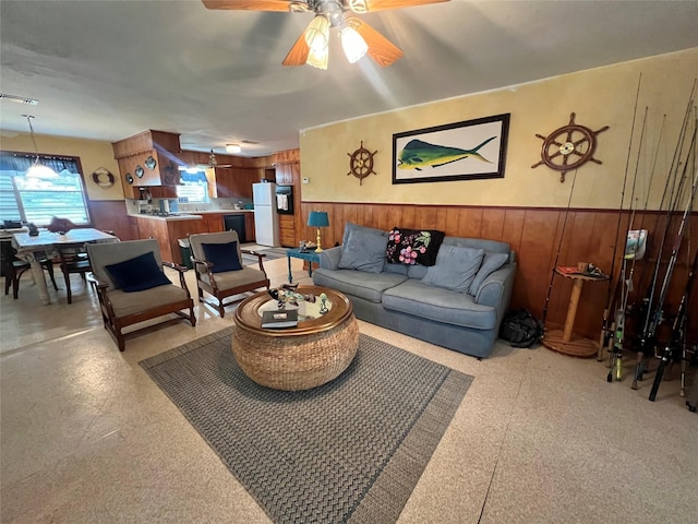 living area featuring wood walls, wainscoting, and ceiling fan