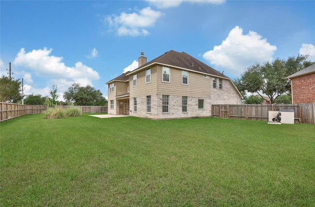 back of house featuring brick siding, a yard, a fenced backyard, and a chimney