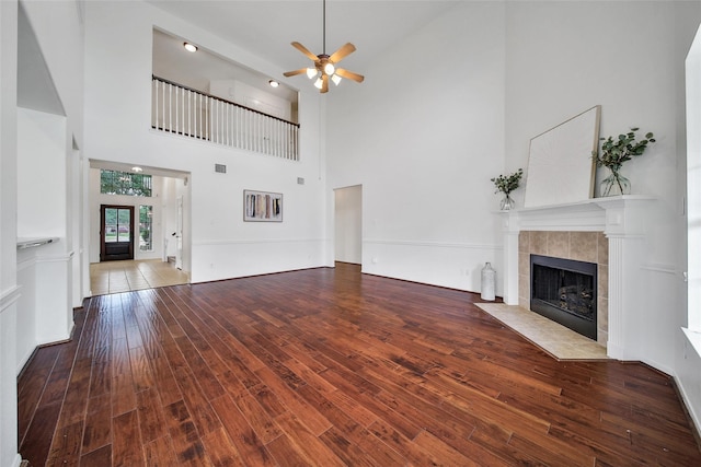 unfurnished living room with wood finished floors, ceiling fan, a high ceiling, and a tile fireplace